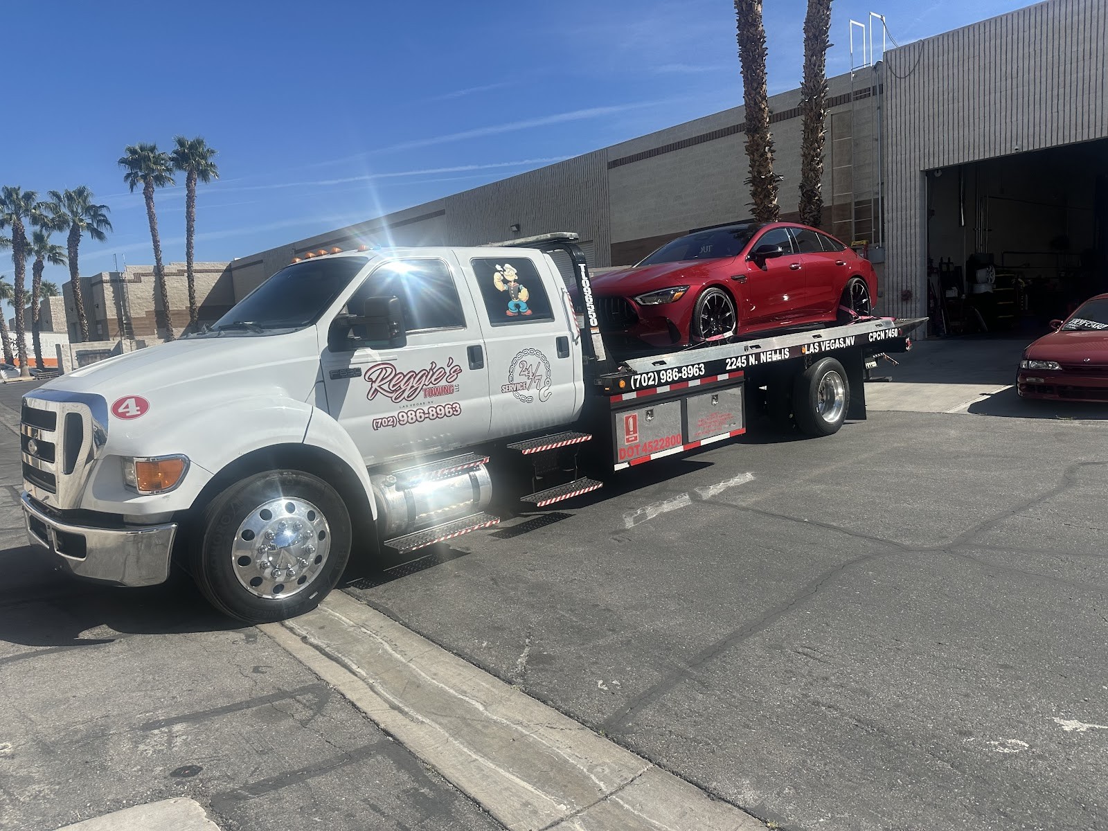Reggie's Towing flatbed carrying a red Mercedes-AMG sedan on a sunny day
