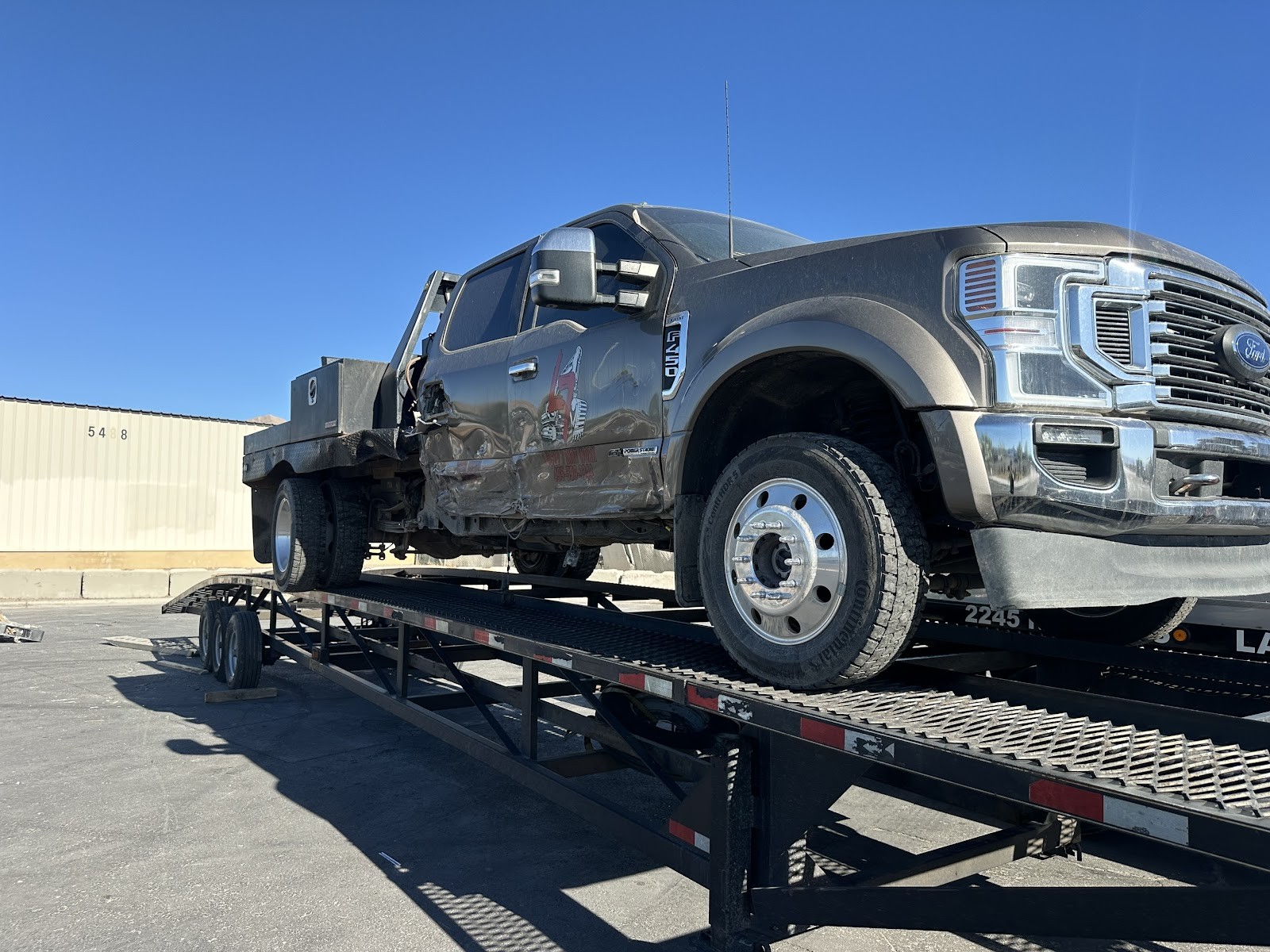 Damaged gray Ford F-450 loaded on a Reggie's Towing gooseneck trailer